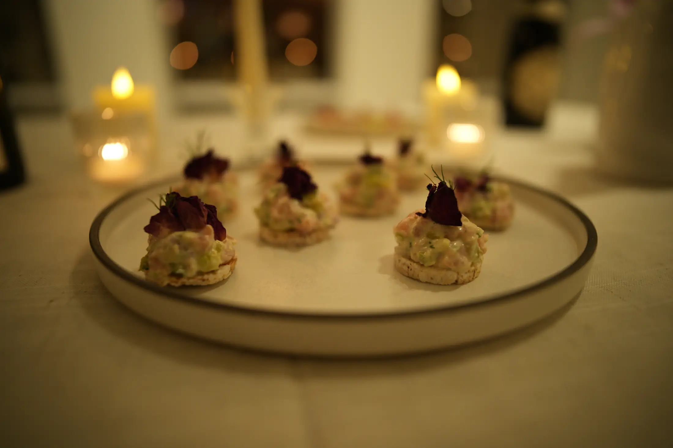 A plate of canapés on the counter, candle flames blurred behind it