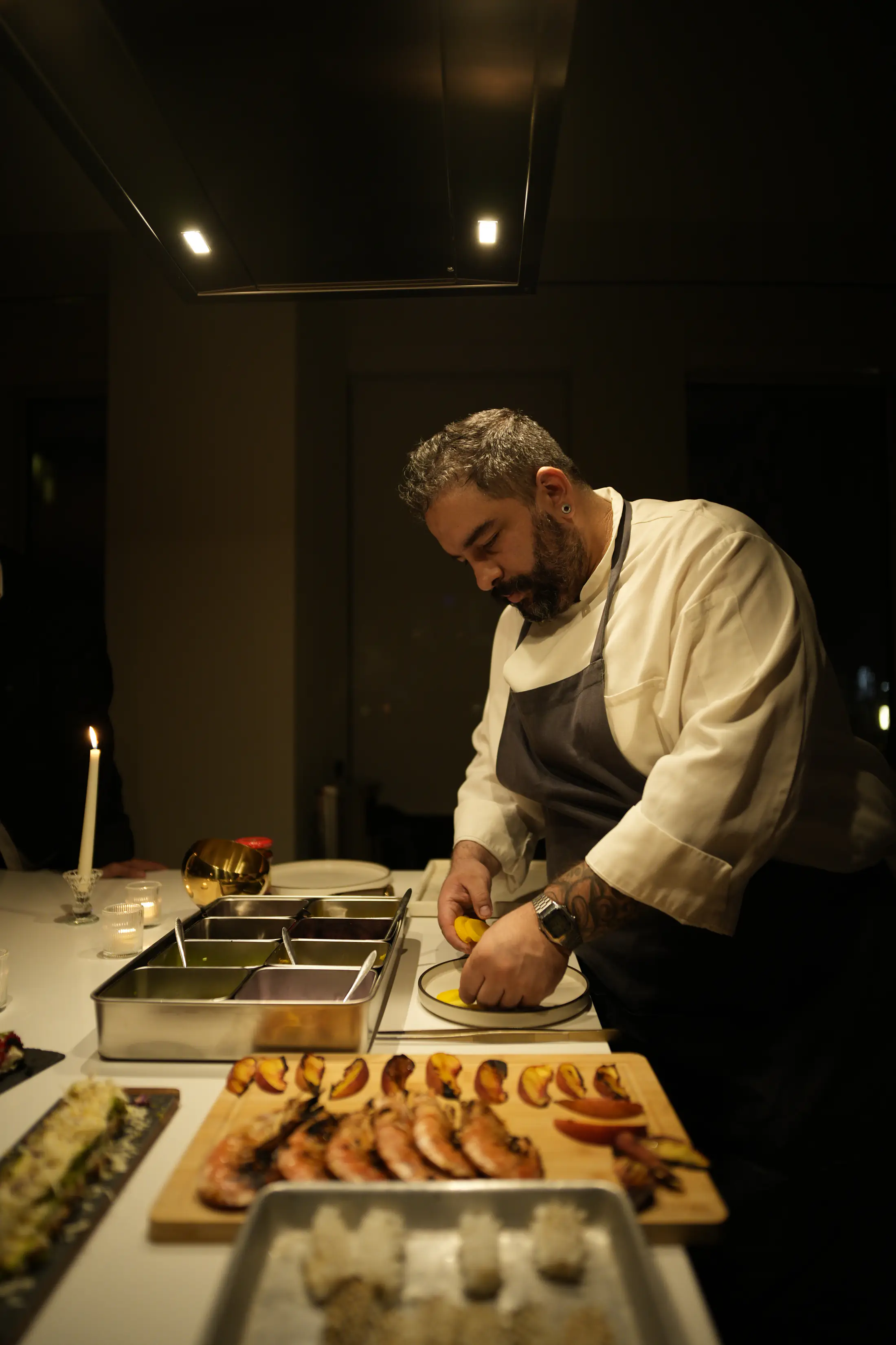 A chef leaning over the counter, squeezing lemon onto a small plate by candlelight